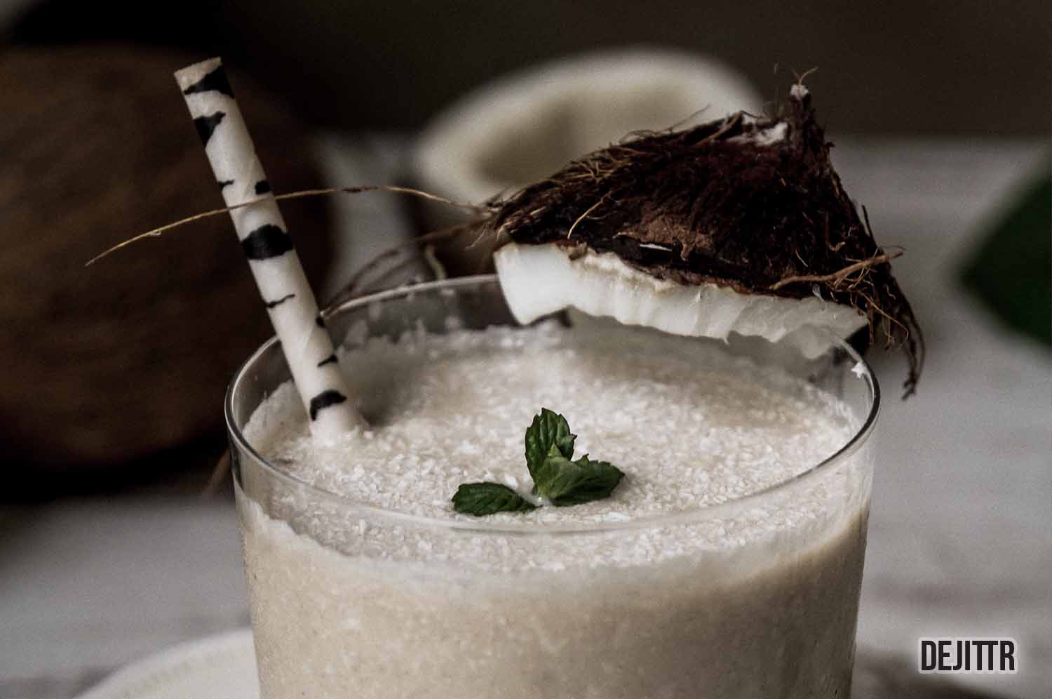 chunky looking coconut milk in a glass cup with a straw and a piece of coconut