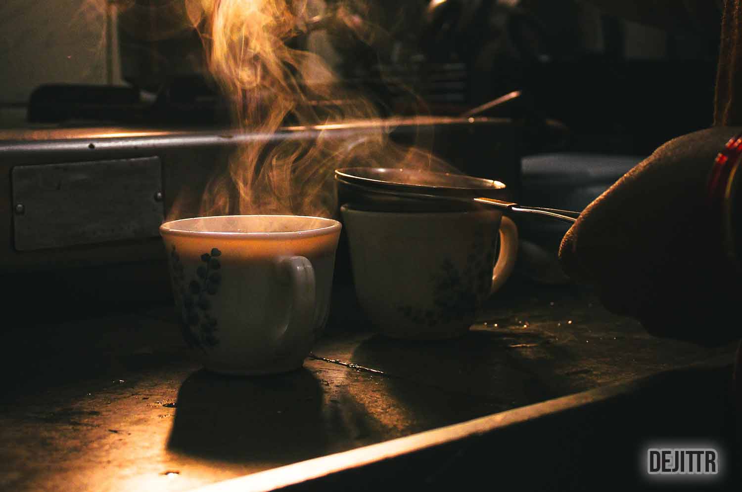 person making masala chai in two white mugs