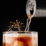 Can Of Energy Drink Pouring Into Glass With Ice And Splashes Of Liquid