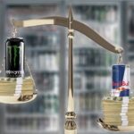 Red bull and monster energy drinks sitting on gold antique scale with stacks of money red bull side heavier