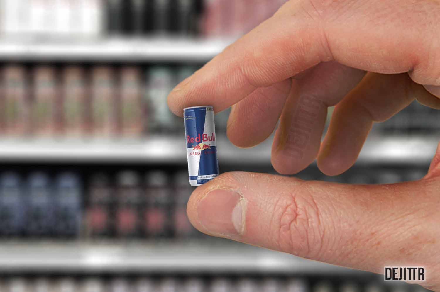 Someone holding a really small can of red bull in finger tips with blurred out shelf of energy drink in the background